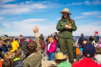 Park ranger in green suit and hat addressing a crowd of visitors