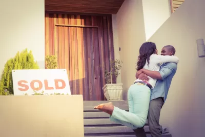 Couple embracing happily in front of home with "SOLD" sign