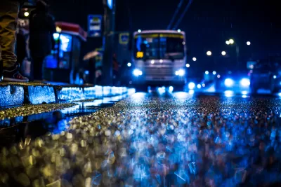 Rainy night in the big city, people standing at the bus stop waiting for the bus. View from the level of asphalt, in blue tones