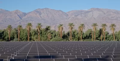 Array of solar panels in the foreground with palm trees and mountains in background, Death Valley, California