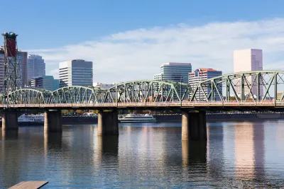 Green steel bridge over Columbia River with Portland, OR skyline in background.
