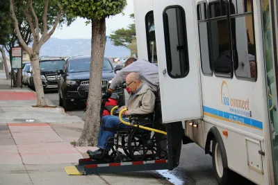 Elderly man in wheelchair exiting white paratransit vehicle.