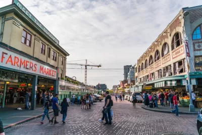 View of stone-paved street with pedestrians and "Farmers Market" neon sign on left and old buildings on right in Seattle, Washington