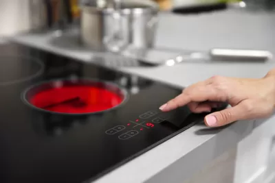 Close-up of black electric stove with red heated coil and person reaching out to press button