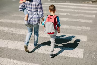 Adult holding small child and holding hand of older child walking across crosswalk