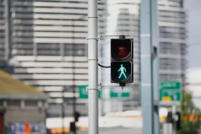 Pedestrian stoplight with green 'walk' silhouette lit up and blurry city buildings in background