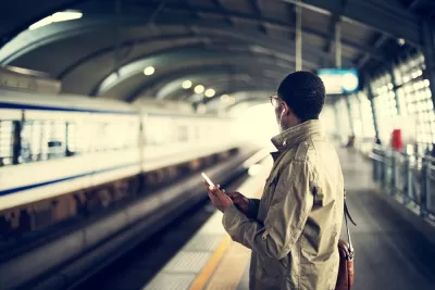 Person on subway platform holds phone and looks toward track