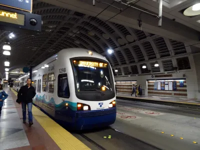 Blue and white Sound Transit light rail train at platform in covered station with man walking towards camera in Seattle, Washington.