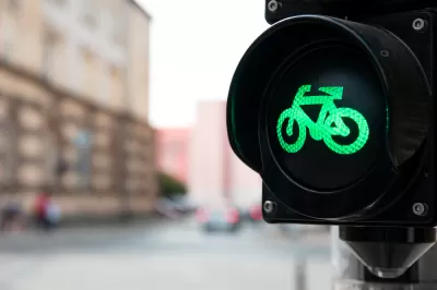 Close-up of black traffic light with green bike symbol lit up and blurry urban scene in background