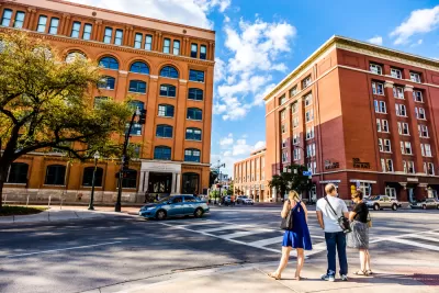 View of Dealey Plaza with pedestrians at crosswalk and brick book depository building in background