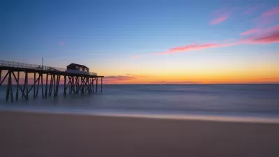 View of empty beach with wooden fishing pier going out into Atlantic Ocean at sunset in New Jersey