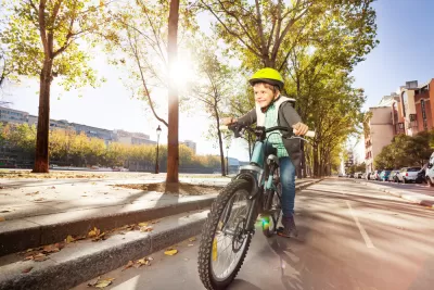 Young boy wearing yellow helmet riding a bicycle down a city street