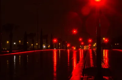 Red street lights on dark, wet-looking road at night.