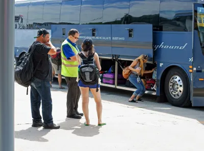 Three passengers and driver stand next to Greyhound bus at station with bottom luggage compartment open.