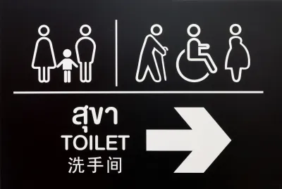 White on black restroom sign with symbols and text in Thai.