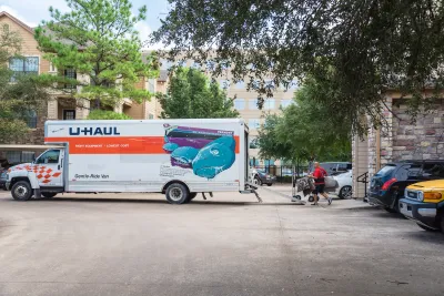 U-Haul moving truck parked perpendicularly in street with man moving furniture into it.