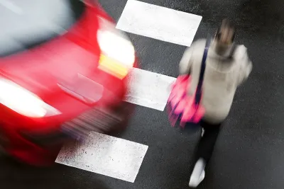 Red car turning into crosswalk as a person walks in front of it.