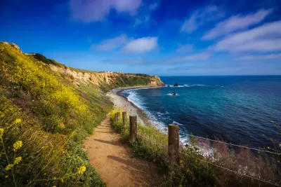 Dirt walking trail with blue ocean on one side and green hillside on the other in Rancho Palos Verdes, California