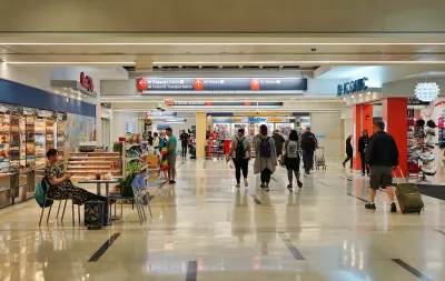 People walk through Philadelphia International Airport. There is a convince store on the right. 