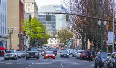 A road in Portland with cars facing the camera and tall buildings on either side. The cars are stopped at a traffic light.