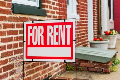 Red and white For Rent sign in front of brick building with flowerpots in background