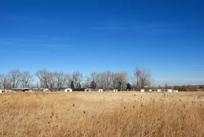 Trailer park and line of bare winter trees in the distance over a golden field on the Colorado prairie.