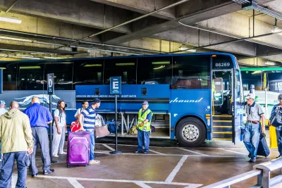 Blue Greyhound bus in a terminal with people with luggage standing next to it.