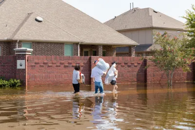Family walking through knee-high flood waters next to brick homes in Houston, Texas.