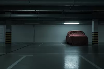 Dark parking garage, empty except for one car covered with a red tarp