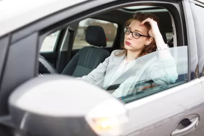 Woman in car stuck in traffic, leaning on her elbow in frustration