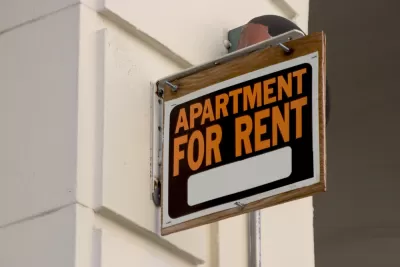 "Apartment for Rent" sign installed perpendicularly on a while building wall