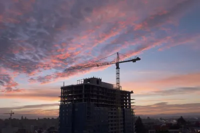 Construction crane next to large building under construction against sunset sky in Seattle, Washington.