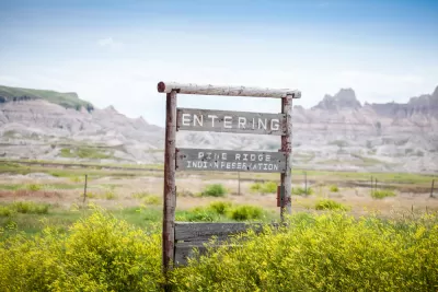 Wooden roadside sign "Entering Pine Ridge Indian Reservation" with mountains in background