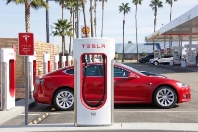 Red Tesla car parked at a Tesla charger at a gas station on a sunny day.