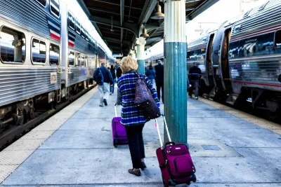 Passengers pulling roller bags on outdoor train platform between trains.