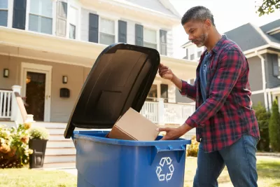 Man dropping cardboard box in blue curbside recycling bin