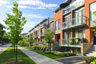 Row of modern red brick townhomes on street with sidewalk and young trees