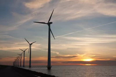 Line of offshore wind turbines with sunset over sea in the background