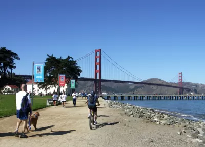 People walking and biking on flat dirt trail next to San Francisco Bay with Golden Gate Bridge in background