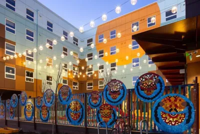 Colorful modern affordable housing apartment building in Seattle, Washington with bistro lights strung across yard at dusk.