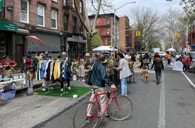 Man with red bicycle walks bike down 'open street' with vendor booths in New York City.