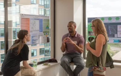 Image of a collaborative conversation between an instructor and students in the corner of a classroom with a large window and posters hung up on the class