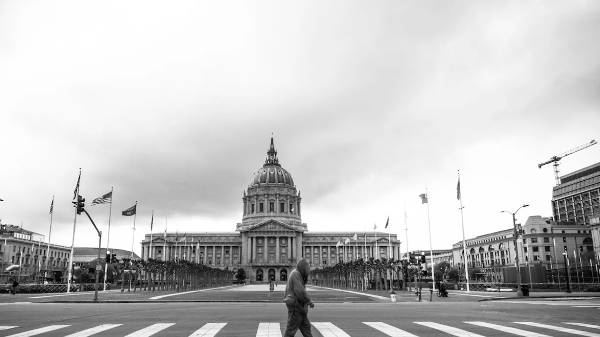 Black and white photo of San Francisco city hall neoclassical dome with person walking across crosswalk in foreground.