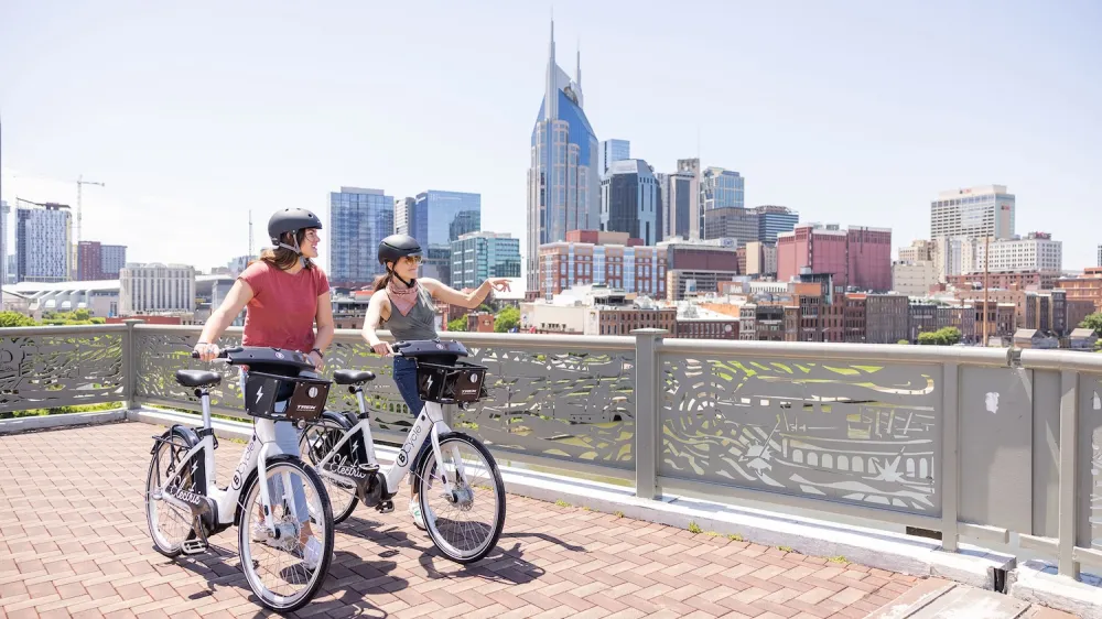 Two people on Nashville BCycle bike share wearing helmets loking out over railing at downtown skyline.