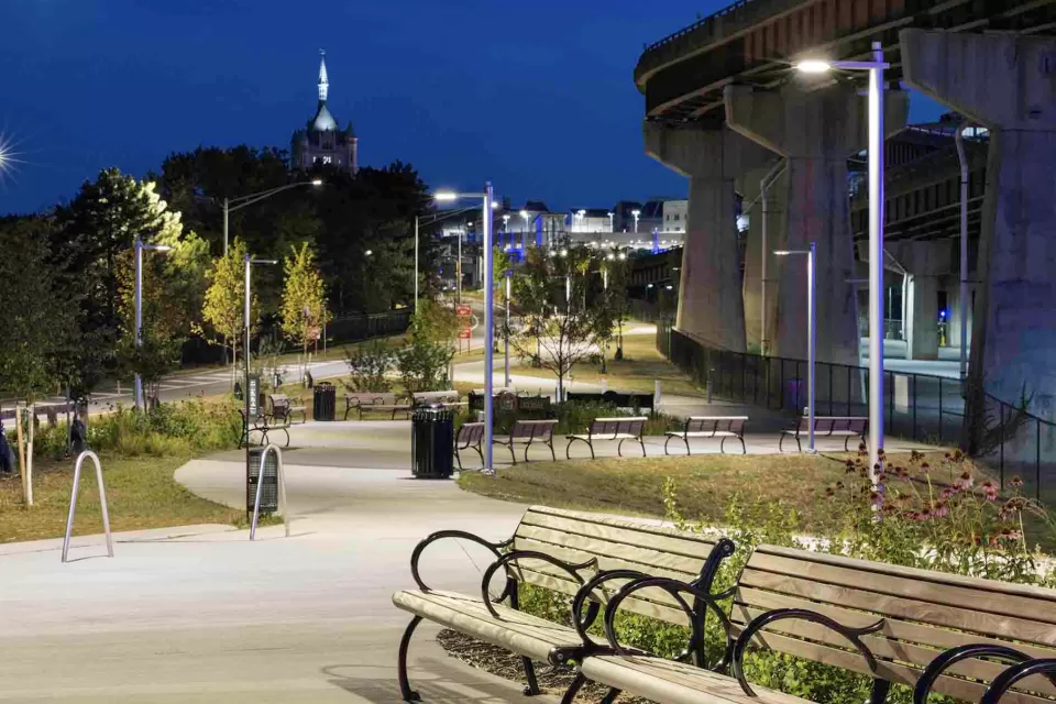 Benches along lit paved bike trail adjacent to freeway overpass in Albany, New York