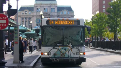 A white RIPTA bus with a bike on a front bike rack at a stop in Providence, Rhode Island.