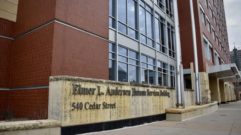 A brick building with windows and a stone plaque that reads "The Elmer L. Andersen Human Services Building"
