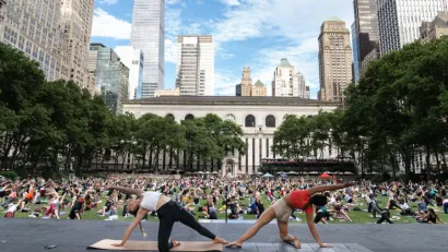 Group of people being led in yoga by two instructors on large public lawn.