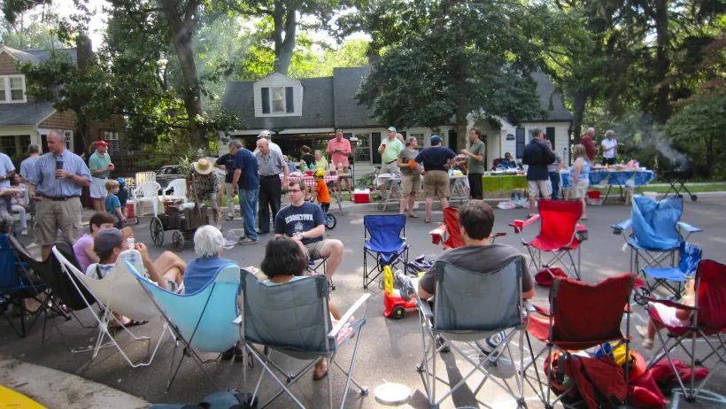 People sitting in lawn chairs on residential street having block party.