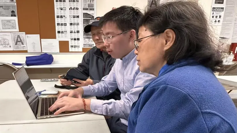 Young Chinese American man helping two seniors sign up for services on a laptop.
